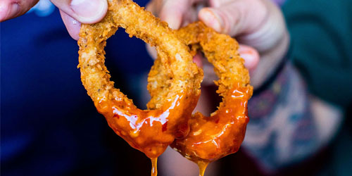 Two People Dipping Onion Rings in Sauce